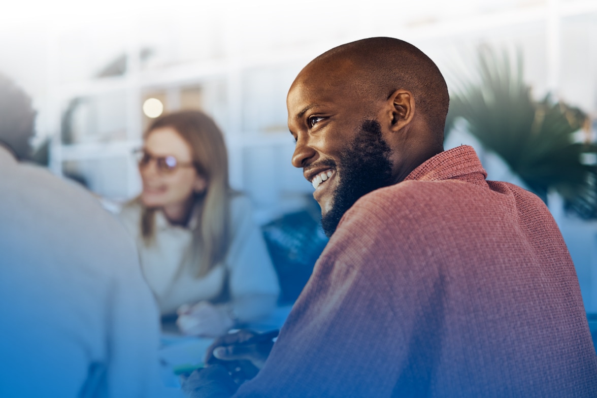 sponsor donate cybersecurity education public awareness cyber tools resources ncf Man smiling and engaged in conversation, with other people blurred in background.